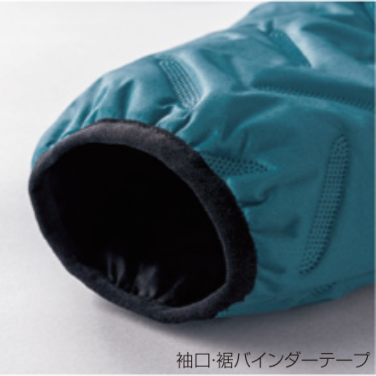クロダルマ 54387 防風中綿ストレッチジャケットの袖口・裾バインダーテープ拡大画像。ターコイズブルーの生地にブラックのバインダーテープを採用し、袖口や裾をすっきり仕上げた秋冬用防寒作業服。建設現場・物流倉庫・配送業・屋外作業などにおすすめ